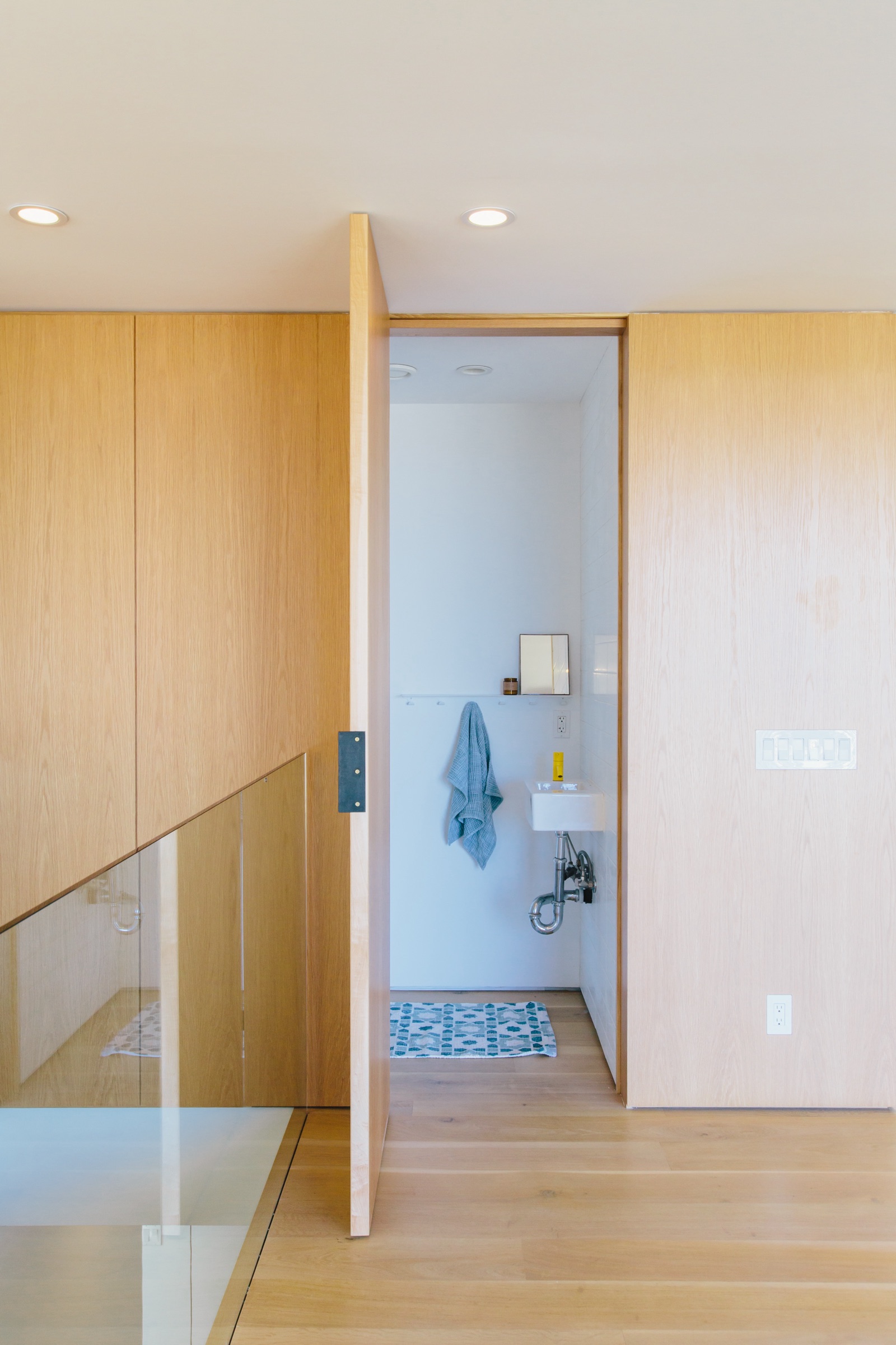 White oak pivot door opening to a small washroom