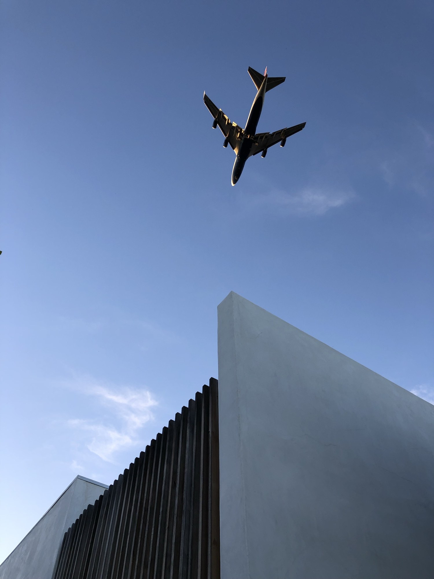Jet passing over the white parapet and slat screen at dusk