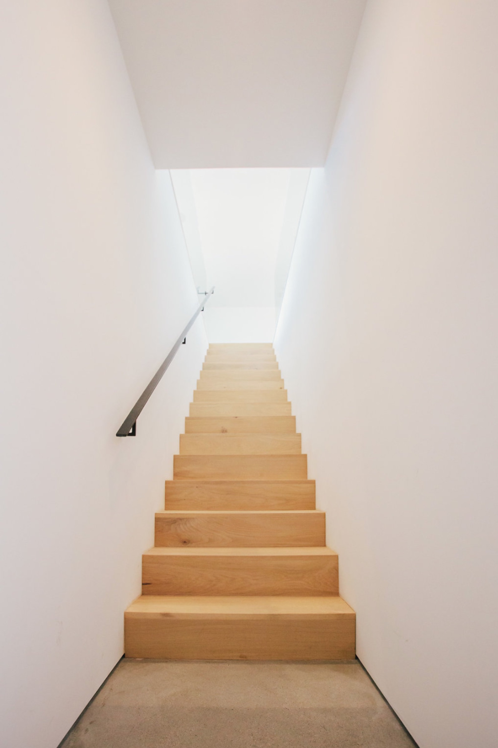 White oak stair rising between white walls with steel handrail