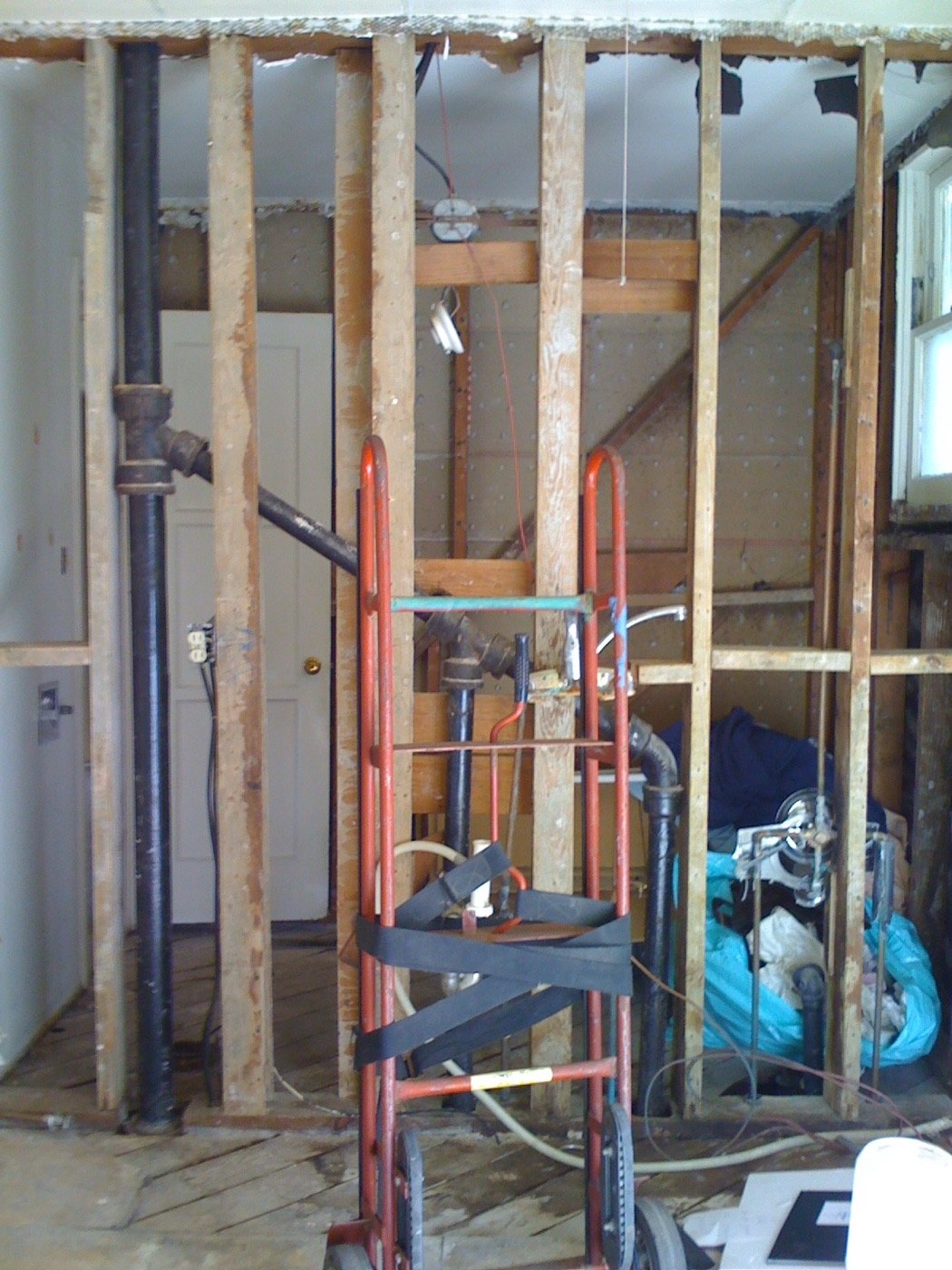 Bathroom wall stripped to framing with ladder and exposed plumbing
