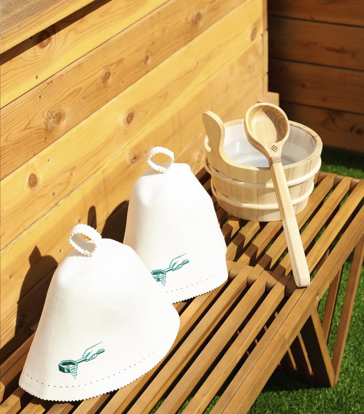 Two felt sauna hats, a birch bucket, and ladle on a slatted table