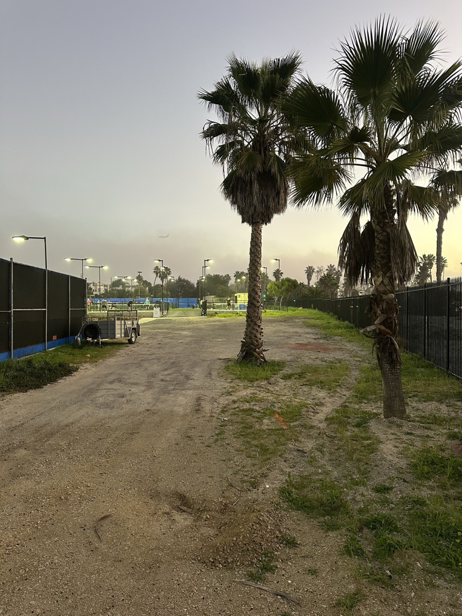 The dirt strip beside the courts at dusk, before the build